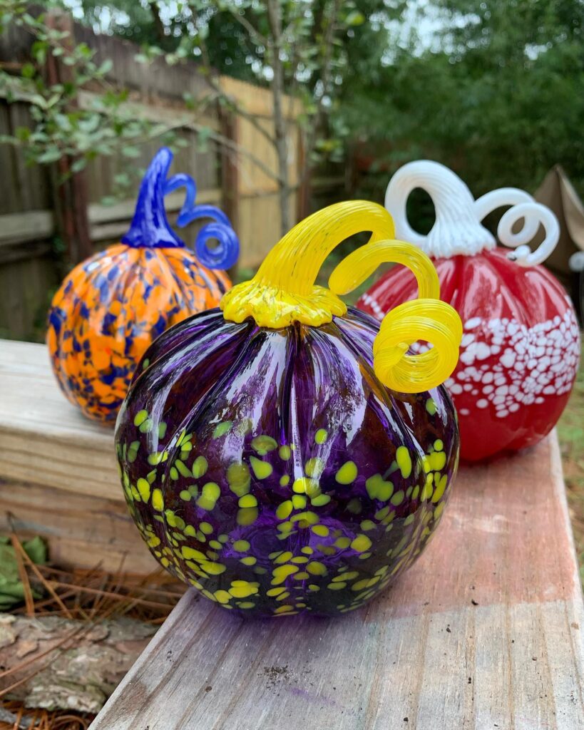 A group of three glass pumpkins sitting on top of a wooden table.