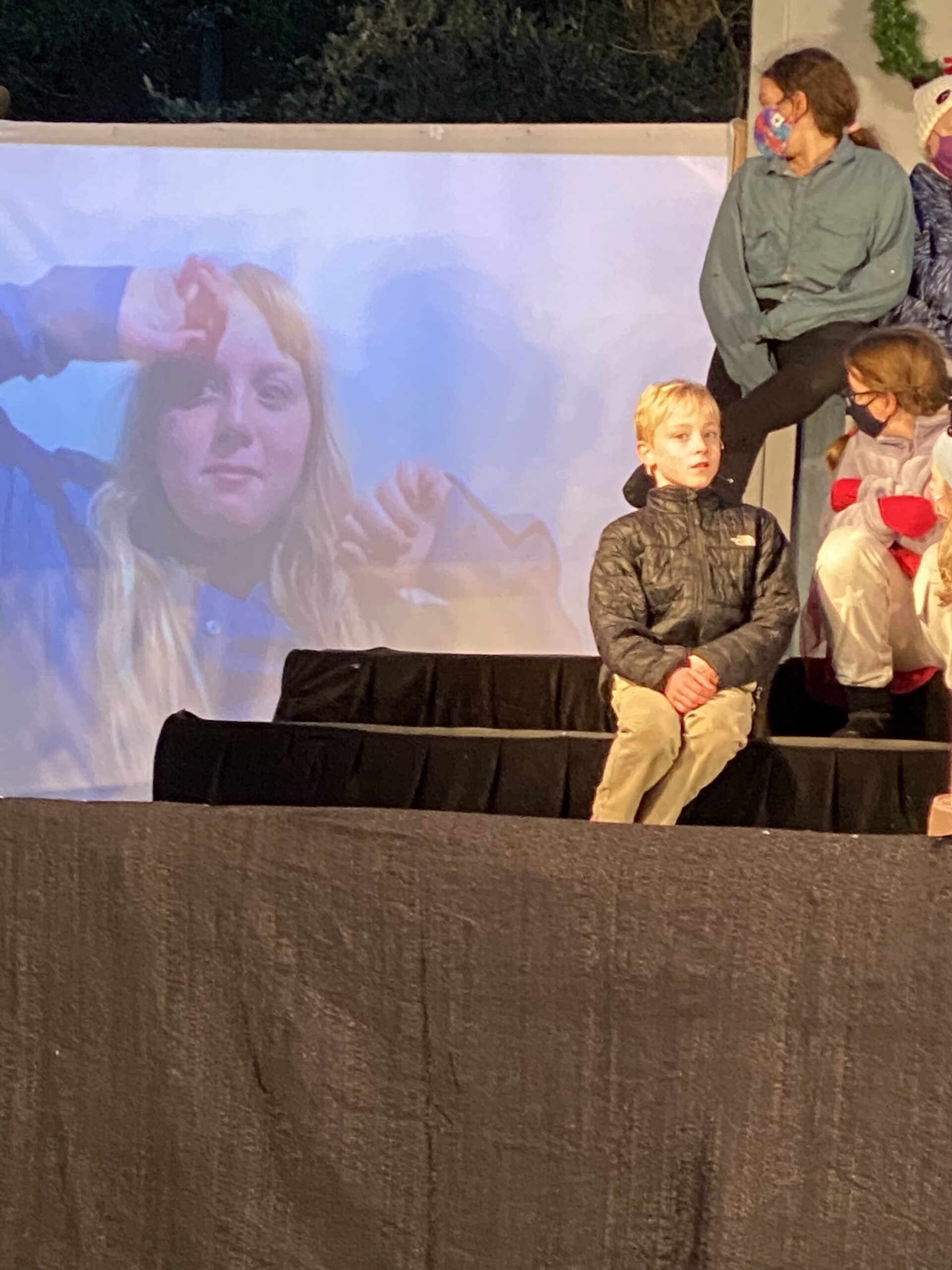 A boy sitting on the stage with his family.