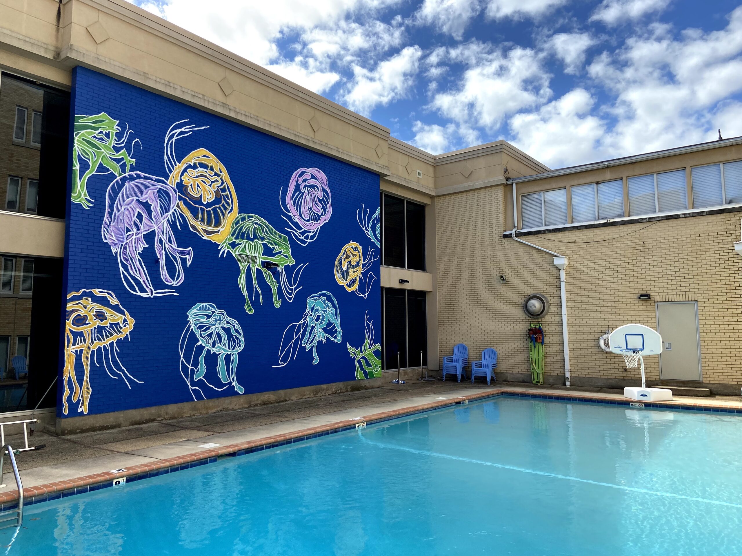 A swimming pool with chairs and a mural on the wall.