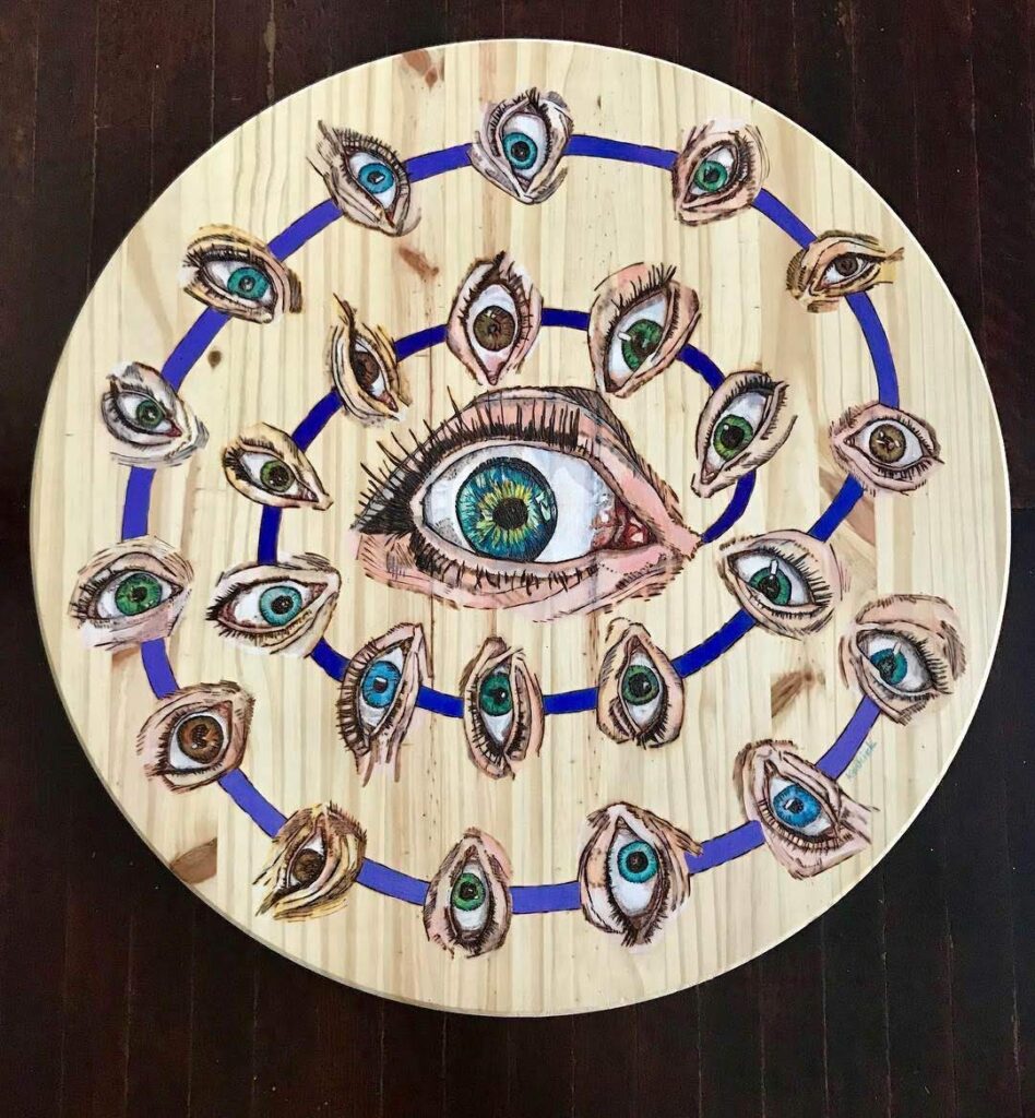 A wooden plate with an eye and peacock feathers on it.