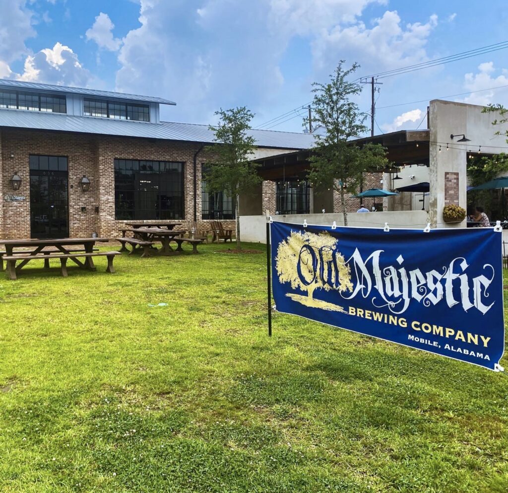 A blue sign sitting in the grass near some picnic tables.