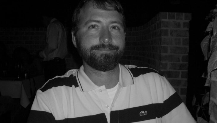 A man with a beard and glasses in black and white.