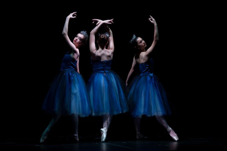 Three women in blue dresses are dancing on a stage.