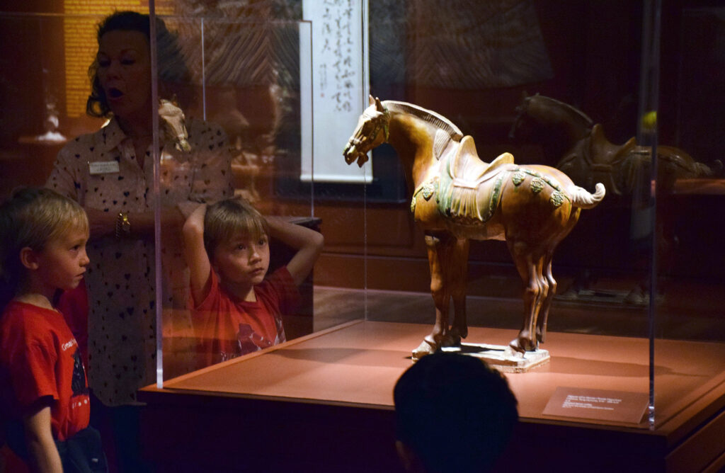 A child looking at a horse statue in a museum.