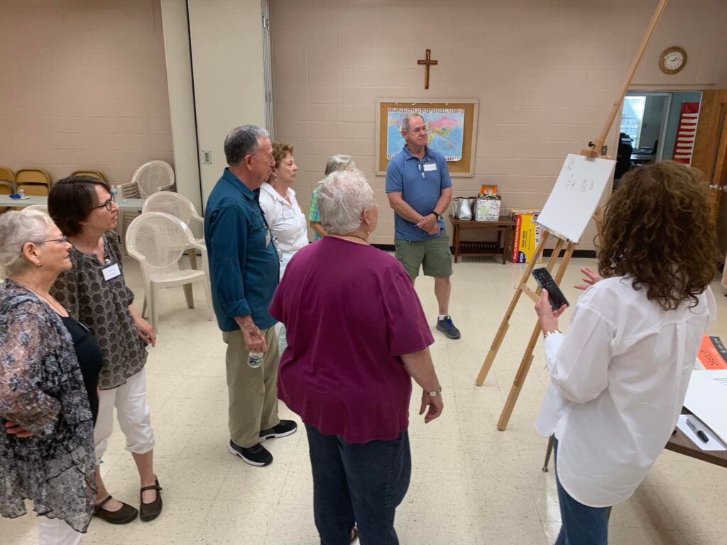 A group of people standing around in front of an easel.